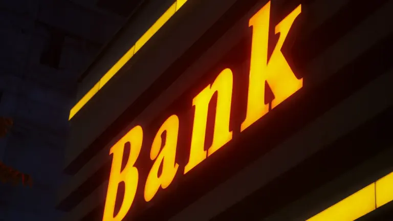 Spilgta, izgaismota bankas izkārtne tumšā fonā, kas simbolizē finanšu institūciju lēmumus.