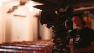 Profesionāla videokamera uz statīva teātra zālē gatavojas Jāņa Streiča jubilejas koncertuzvedumam.