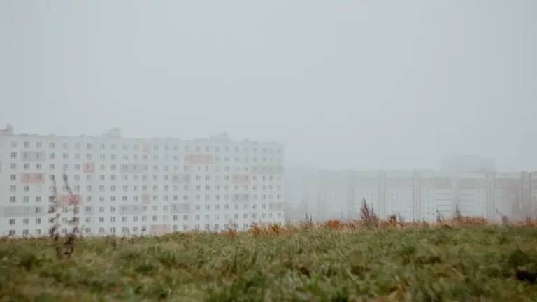 Daudzdzīvokļu nams Rīgā miglainā laikā, kas simbolizē nekustamā īpašuma nodokļa neskaidrības.
