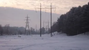 Augstsprieguma līnijas sniegotā Latvijas ainavā ziemas periodā, simbolizējot valsts enerģētikas infrastruktūru.