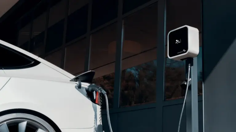 Balts elektroauto lādējas pie modernās uzlādes stacijas pilsētas vidē vai mājās.