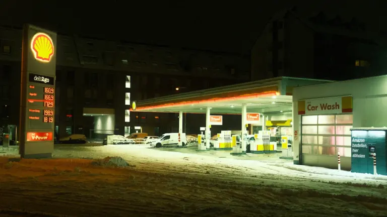 Degvielas uzpildes stacija vakarā ar sniegu un norādītām degvielas cenām uz tablo