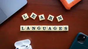 Vārdi 'Learn Languages', kas salikti no skrābļa spēles kauliņiem uz koka galda.