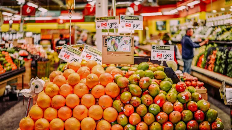 Augļu un dārzeņu stends lielveikalā ar cenu zīmēm un svaigu produkciju