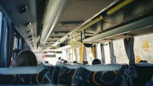 Skatoties no autobusa salona uz priekšu, redzamas pasažieru sēdvietas Rīgas sabiedriskajā transportā.