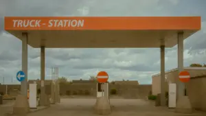 Degvielas uzpildes stacija ar uzrakstu Truck Station zem mākoņainas debess.